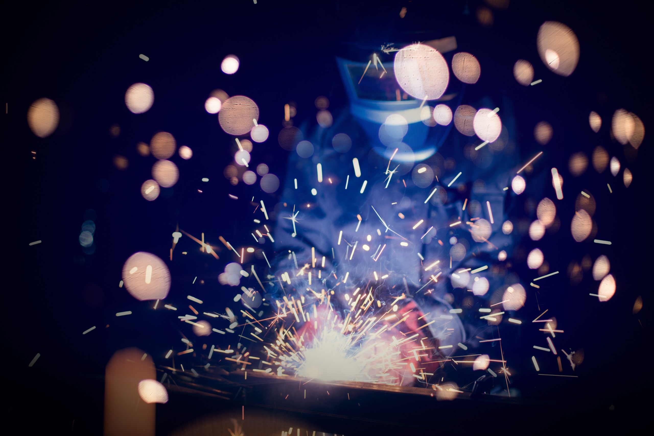 Employee welding steel with sparks using mig mag welder – focus on sparks.